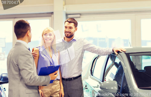 Image of happy couple with car dealer in auto show or salon