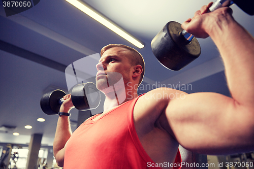 Image of young man with dumbbells flexing muscles in gym