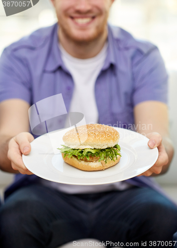 Image of close up of man holding hamburger on plate at home