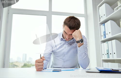 Image of stressed businessman with papers in office