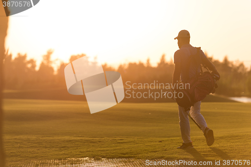 Image of golfer  walking and carrying golf  bag at beautiful sunset