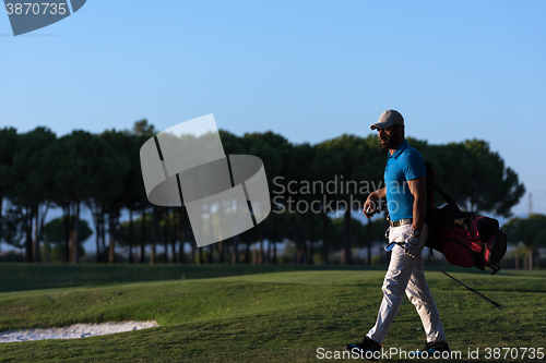 Image of golfer  walking and carrying golf  bag at beautiful sunset