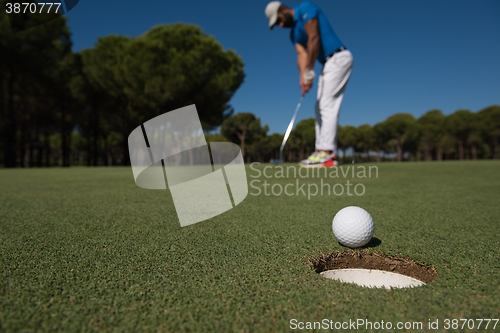 Image of golf player hitting shot, ball on edge of hole