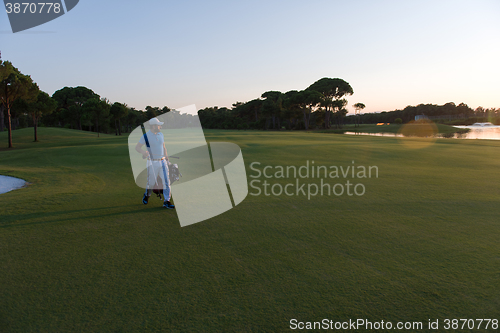 Image of golfer  walking and carrying golf  bag at beautiful sunset