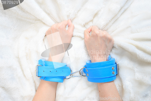Image of female hands in blue leather handcuffs. eagerly grabbed the sheets.. sex toys.