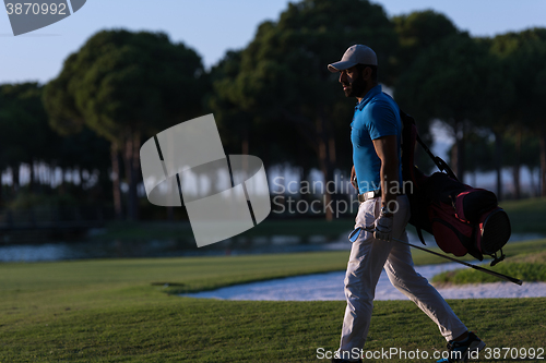 Image of golfer  walking and carrying golf  bag at beautiful sunset