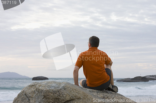 Image of Man sitting on a rock at the sea