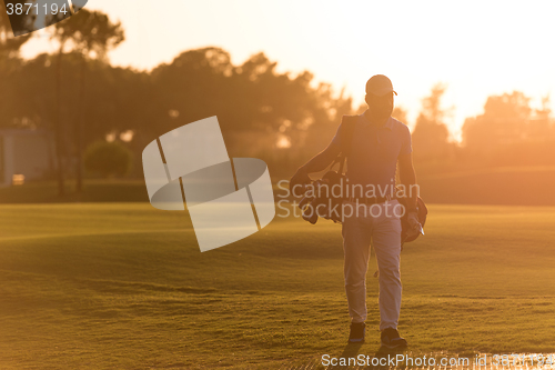 Image of golfer  walking and carrying golf  bag at beautiful sunset