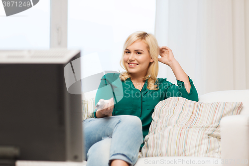 Image of smiling woman with remote watching tv at home