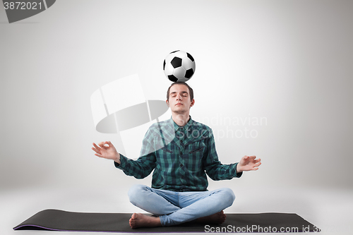 Image of Portrait  of young man, practicing yoga with football ball