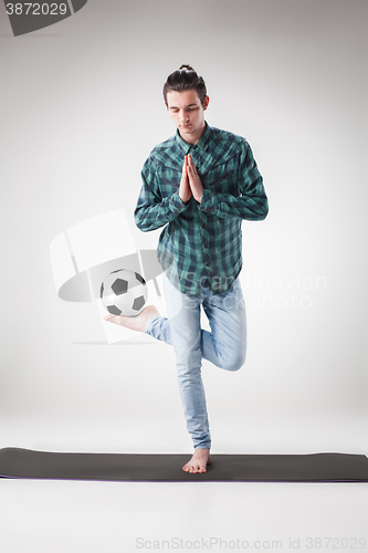 Image of Portrait  of young man, practicing yoga with football ball