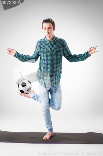 Image of Portrait  of young man, practicing yoga with football ball