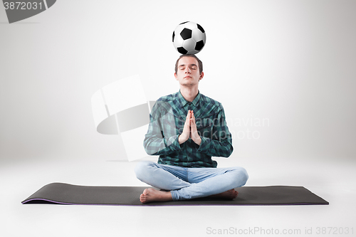 Image of Portrait  of young man, practicing yoga with football ball