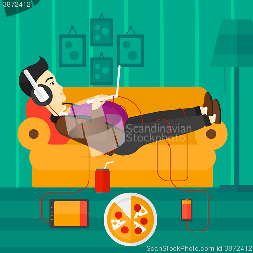 Image of Man lying on sofa with many gadgets.