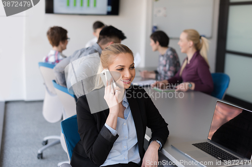 Image of business woman speeking on phone at office with team on meeting 