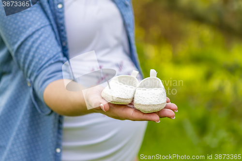 Image of close up of pregnant woman hand with baby shoes 