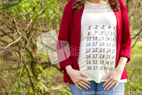 Image of Pregnant woman in red jacket with calendar on her T-shirt outdoo