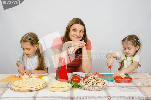 Image of Mom sits at the kitchen table with a dreamy view of two little girls close concentration cut products