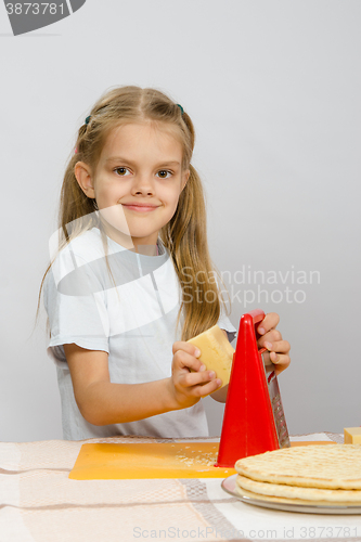 Image of Six-year girl posing at the kitchen table with cheese and a grater in the hands of