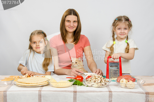 Image of Mother and two little girls at a table prepared ingredients for the pizza. They were watching a cat