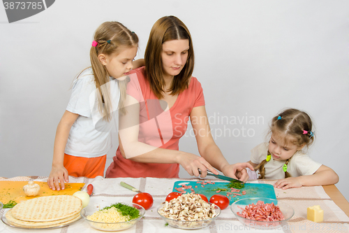 Image of Two daughters are watching with interest as the mother chopped green