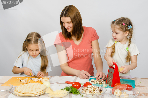 Image of Mum with a five-year daughter watched as the eldest daughter cutting mushrooms pizza