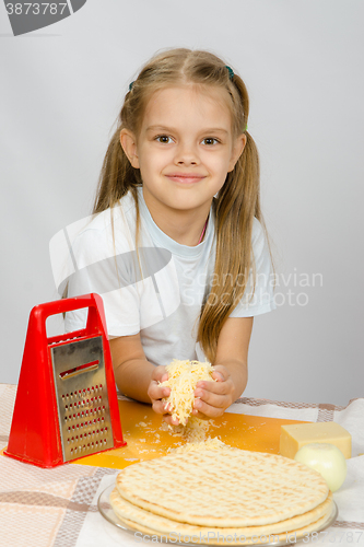 Image of The little girl at the table rubbed grated cheese for pizza