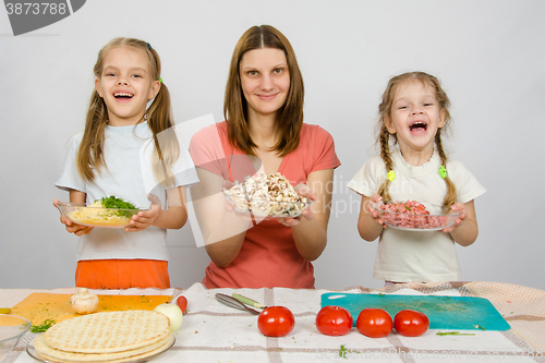 Image of Mother with two daughters happily holding a plate with sliced products for pizza