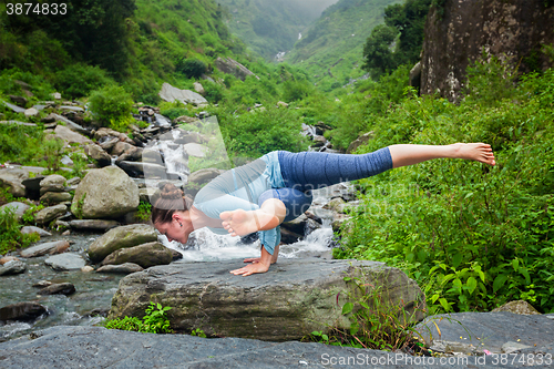 Image of Woman doing yoga oudoors at tropical waterfall