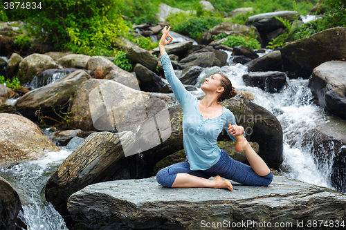 Image of Woman doing yoga outdoors at tropical waterfall