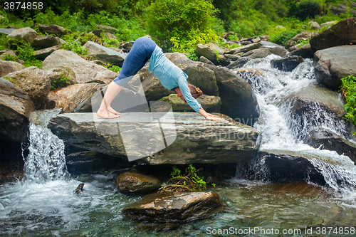 Image of Woman doing yoga oudoors at tropical waterfall