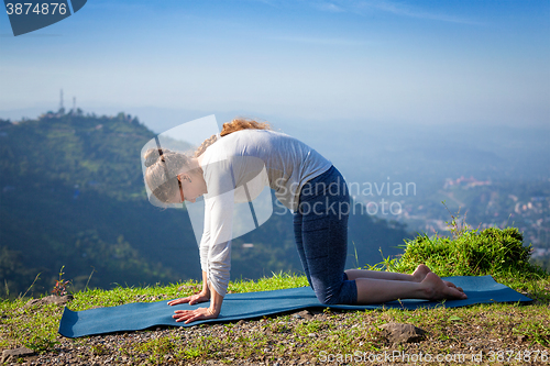 Image of Woman practices yoga asana Marjariasana outdoors