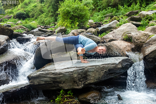 Image of Woman doing yoga oudoors at tropical waterfall