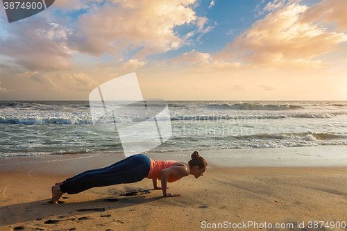 Image of Woman practices yoga  at the beach on sunset