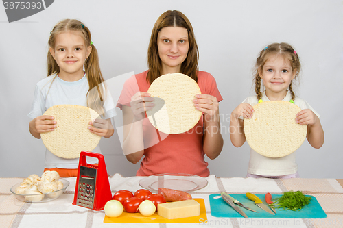 Image of Mum with two little girls sitting in a row at the kitchen table and a hand-held pizza bases