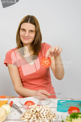 Image of The girl at the kitchen table holding two fingers chopped tomato circle