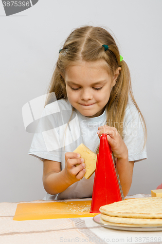 Image of Six-year girl posing at the kitchen table with cheese and a grater in the hands of