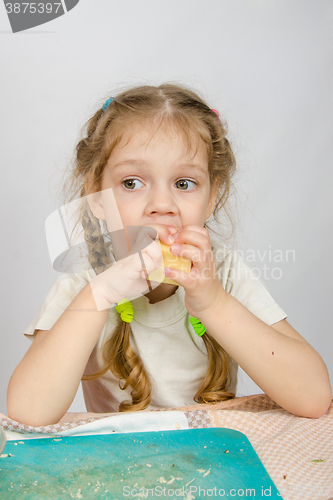 Image of Six-year girl with pigtails trying to bite off a piece of cheese that keeps both hands