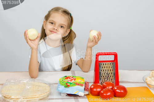 Image of Six year old girl at the kitchen table having fun holding vegetables