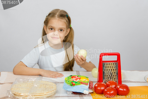 Image of Six-year girl sitting at the kitchen table in front of her are vegetables, base and other ingredients for pizza