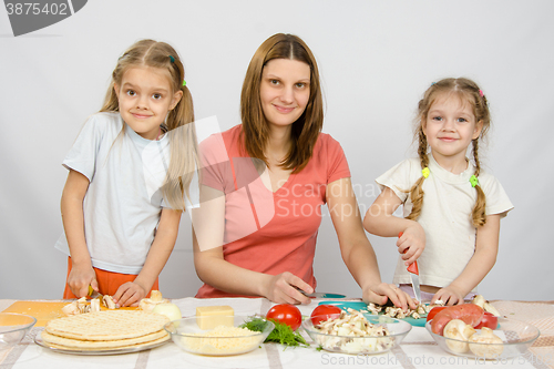 Image of Woman with two young girls at the table prepared ingredients for pizza