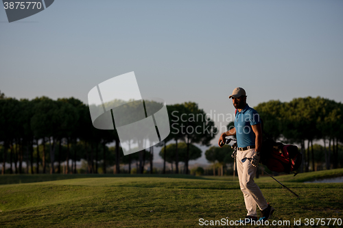 Image of golfer  walking and carrying golf  bag at beautiful sunset