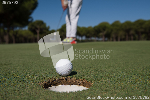 Image of golf player hitting shot, ball on edge of hole