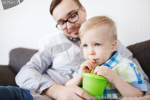 Image of father and son drinking from cup at home