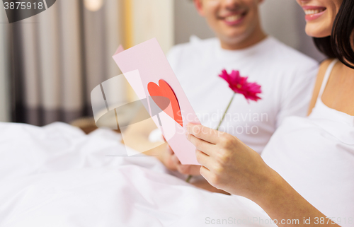 Image of close up of couple in bed with postcard and flower