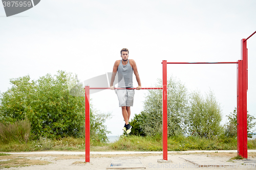 Image of young man exercising on horizontal bar outdoors