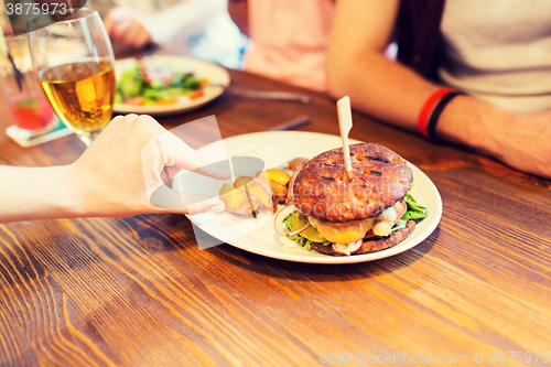 Image of close up of friends hands sharing burger at bar