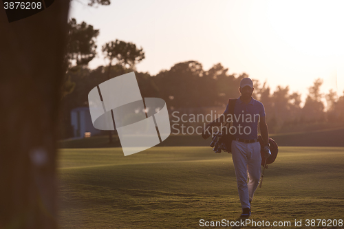 Image of golfer  walking and carrying golf  bag at beautiful sunset