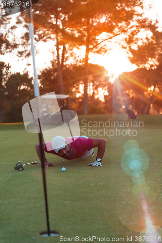 Image of golf player blowing ball in hole with sunset in background