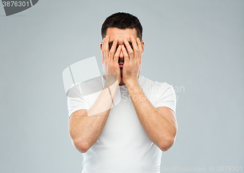 Image of man in white t-shirt covering his face with hands